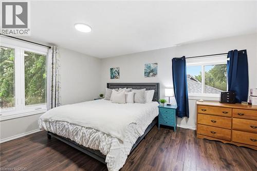 Bright and spacious bedroom featuring a dark-framed bed, wood-finish flooring throughout, and abundant natural light from dual windows with operable glass doors - 450 East 42Nd Street, Hamilton, ON - Indoor Photo Showing Bedroom
