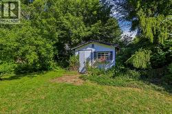 Detached storage shed with white siding and dark shutters - 