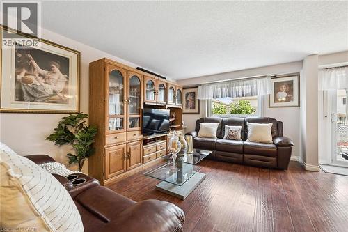 Spacious living area showcasing rich wood-finish flooring, built-in cabinetry with glass-front display shelving, and a leather sectional sofa arrangement - 86 Bridlewreath Street, Kitchener, ON - Indoor Photo Showing Living Room