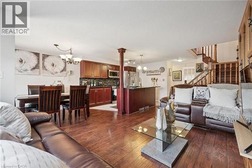 Open-concept living space featuring wood-finish flooring, a kitchen with dark cabinetry and a tile backsplash, a dining area with a chandelier, and a staircase with wood railings - 86 Bridlewreath Street, Kitchener, ON - Indoor Photo Showing Living Room