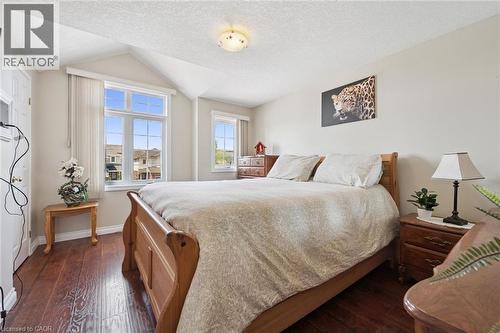 Spacious bedroom featuring hardwood flooring, a wood-frame bed, dual nightstands with task lighting, and abundant natural light from large multi-pane windows with custom drapery - 86 Bridlewreath Street, Kitchener, ON - Indoor Photo Showing Bedroom