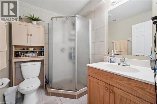 Spa-inspired primary bathroom featuring a corner walk-in shower with frosted glass enclosure and chrome fixtures, wood-finish vanity with white countertop and integrated sink, large mirror with integr - 86 Bridlewreath Street, Kitchener, ON - Indoor Photo Showing Bathroom