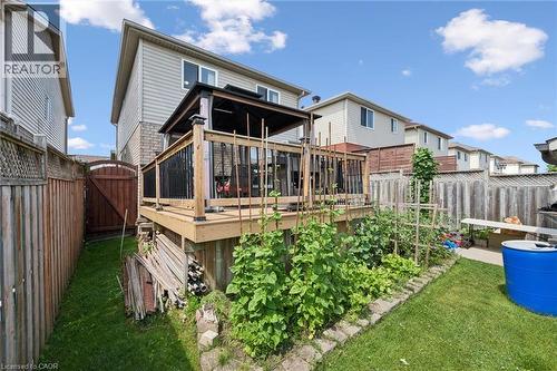 Spacious backyard oasis featuring a composite deck with black metal railings, lush mature landscaping with vegetable garden beds, manicured lawn, and detached storage structures - 86 Bridlewreath Street, Kitchener, ON - Outdoor With Deck Patio Veranda