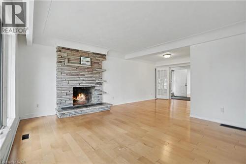 Living area featuring a stone-clad fireplace, light wood-finish flooring, white walls, and bright overhead lighting - 100 Hardale Crescent, Hamilton, ON - Indoor Photo Showing Living Room With Fireplace
