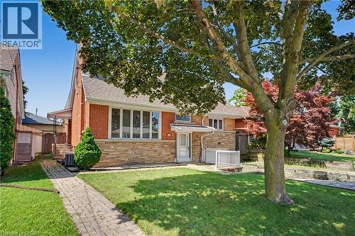 Brick and stone facade residence featuring a front lawn with mature trees, paved walkway, and a covered side entrance - 100 Hardale Crescent, Hamilton, ON - Outdoor