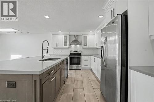 Modern kitchen featuring a large island with an undermount sink, stainless steel appliances, white shaker cabinetry, a subway tile backsplash, and light-toned tile flooring - 100 Hardale Crescent, Hamilton, ON - Indoor Photo Showing Kitchen With Double Sink With Upgraded Kitchen