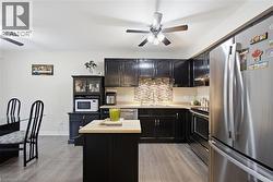 Kitchen featuring dark cabinetry, light countertops, a textured tile backsplash, stainless steel appliances, and wood-finish flooring - 