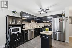 Kitchen featuring dark wood cabinetry, stainless steel appliances, light-toned countertops, and a patterned tile backsplash - 