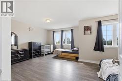 Spacious room featuring wood-finish flooring, light neutral wall tones, and multiple windows with dark window treatments - 