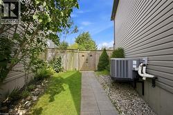 Spacious side yard featuring a manicured lawn, mature landscaping with evergreen shrubs, composite patio pavers, gravel pathways, and modern gray fiber cement siding with integrated HVAC unit and util - 