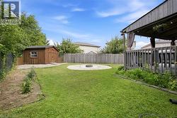 Expansive green lawn with a circular gravel fire pit area, a wooden storage shed, privacy fencing, and a covered wood deck - 
