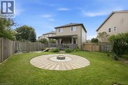 Expansive backyard featuring a circular paver patio with a central fire pit, mature green lawn, and a privacy fence - 