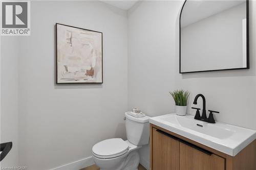 Modern powder room featuring a wood-finish vanity with an integrated white sink, matte black faucet, and an arched wall mirror - 325 Queensdale Avenue E, Hamilton, ON - Indoor Photo Showing Bathroom