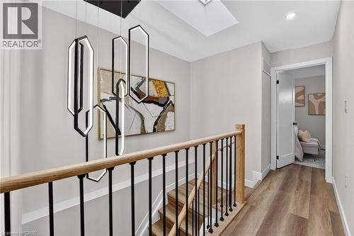 Upper-level hallway featuring a modern chandelier, wood-finish flooring, a skylight, and a staircase with a wood handrail and black metal balusters - 325 Queensdale Avenue E, Hamilton, ON - Indoor Photo Showing Other Room