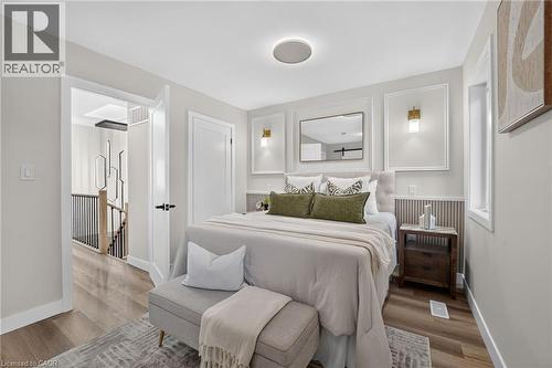 Light-filled room featuring wood-finish flooring, a contemporary ceiling light fixture, a built-in wall sconce, and a framed mirror - 325 Queensdale Avenue E, Hamilton, ON - Indoor Photo Showing Bedroom