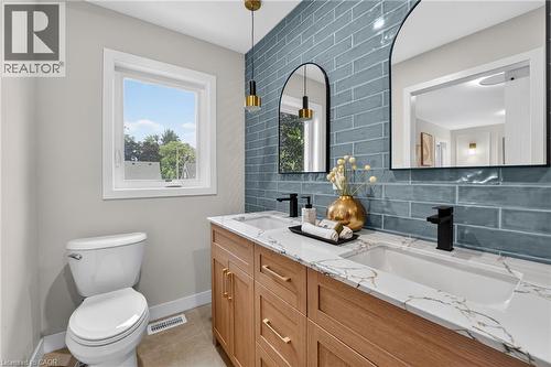 Bathroom featuring a dual vanity with wood-finish cabinetry, white countertops with veining, and matte black fixtures - 325 Queensdale Avenue E, Hamilton, ON - Indoor Photo Showing Bathroom