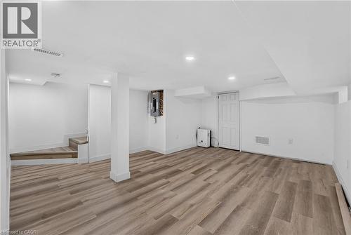 Finished lower level featuring wood-finish flooring, recessed lighting, white walls, a utility door, and staircase access - 325 Queensdale Avenue E, Hamilton, ON - Indoor Photo Showing Other Room