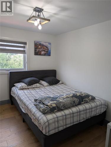 Comfortable bedroom featuring a black upholstered bed frame, plaid bedding, wood-finish flooring, and a ceiling-mounted light fixture - 466 Bankside Drive, Kitchener, ON - Indoor Photo Showing Bedroom