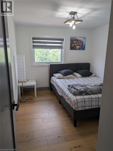 Comfortable bedroom featuring a wood-finish floor, large window with cellular shade allowing natural light, black upholstered bed frame, nightstand with attached lamp, ceiling-mounted light fixture, a - 466 Bankside Drive, Kitchener, ON - Indoor Photo Showing Bedroom