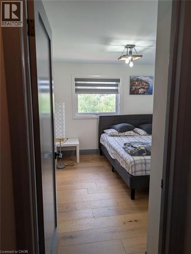 Cozy bedroom featuring a wood-finish plank floor, black upholstered bed frame, and a horizontal window with cellular shade allowing natural light - 466 Bankside Drive, Kitchener, ON - Indoor Photo Showing Bedroom