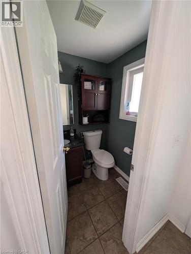 Compact half bath featuring a two-piece toilet, pedestal sink, dark tile flooring, and rich burgundy cabinetry with upper shelving - 466 Bankside Drive, Kitchener, ON - Indoor Photo Showing Bathroom