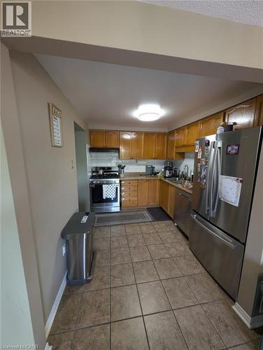 Galley-style kitchen featuring wood-finish cabinetry, stainless steel appliances including a French-door refrigerator, gas range, and tile flooring throughout - 466 Bankside Drive, Kitchener, ON - Indoor Photo Showing Kitchen