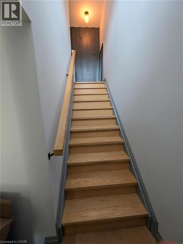 Wood-finish staircase with light gray walls, a contrasting dark gray accent wall, a wall-mounted wood-finish handrail, and a contemporary ceiling light fixture - 466 Bankside Drive, Kitchener, ON - Indoor Photo Showing Other Room