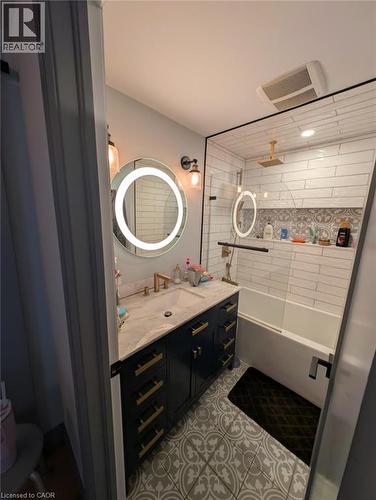 Bathroom featuring a dark blue vanity with gold-tone hardware, a white countertop with an integrated sink, and an illuminated circular mirror - 466 Bankside Drive, Kitchener, ON - Indoor Photo Showing Bathroom