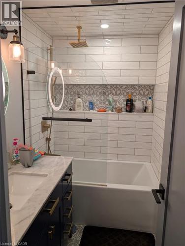 Modern bathroom featuring a white subway tile surround with decorative tile accents, a freestanding soaking tub, floating vanity with dark cabinetry and white countertop, integrated shelving niche wit - 466 Bankside Drive, Kitchener, ON - Indoor