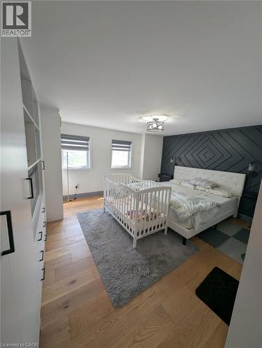 Spacious primary bedroom suite featuring hardwood flooring, dual windows with natural light, a geometric accent wall with modern paneling, ceiling-mounted lighting fixture, and an adjoining nursery sp - 466 Bankside Drive, Kitchener, ON - Indoor Photo Showing Bedroom