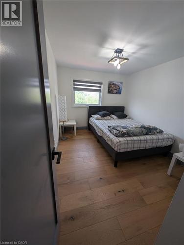 Bedroom featuring wood-finish flooring, a black platform bed frame, striped window treatment with natural light, ceiling-mounted light fixture, and convenient bedside surface - 466 Bankside Drive, Kitchener, ON - Indoor Photo Showing Bedroom