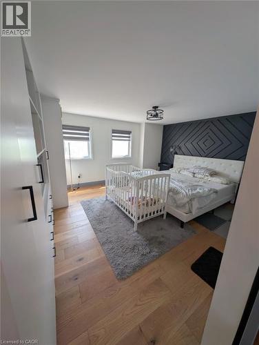 Bright bedroom featuring wood-finish flooring, built-in shelving, dual windows, a decorative wall accent, and a flush-mount ceiling light fixture - 466 Bankside Drive, Kitchener, ON - Indoor Photo Showing Bedroom