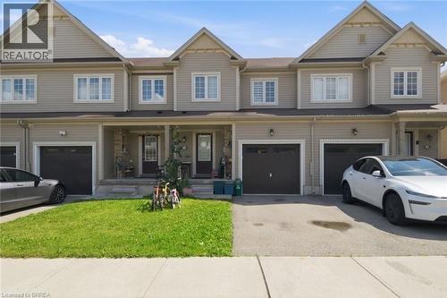 Two-story townhome exterior featuring light beige siding, white-trimmed windows, and dark garage doors - 32 Cole Crescent, Brantford, ON - Outdoor With Facade