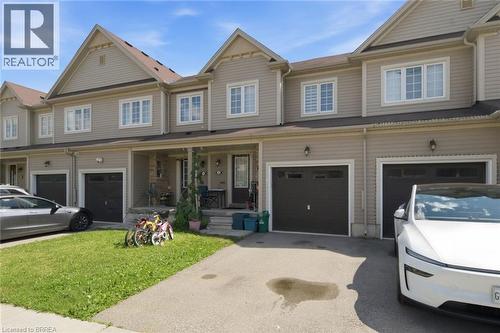 Townhome exterior featuring light beige horizontal siding and contrasting dark brown garage doors - 32 Cole Crescent, Brantford, ON - Outdoor With Facade