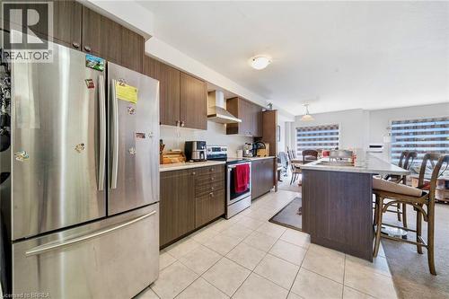Contemporary kitchen featuring dark wood-finish cabinetry, stainless steel appliances, a center island with a stone-finish countertop, and tile flooring - 32 Cole Crescent, Brantford, ON - Indoor Photo Showing Kitchen
