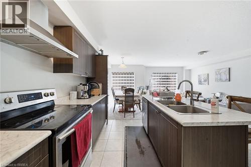 Modern kitchen featuring dark wood-finish cabinetry, light-toned countertops, tile flooring, stainless steel range with overhead vent hood, and a double basin sink with a high-arch faucet - 32 Cole Crescent, Brantford, ON - Indoor Photo Showing Kitchen With Double Sink