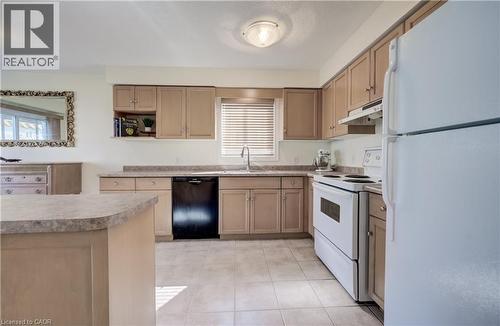 Kitchen featuring a curved peninsula with counter seating, a stainless steel sink with a window above, wood-finish cabinetry, a black dishwasher, and a white electric range with an overhead hood - 496 Langlaw Drive, Cambridge, ON - Indoor Photo Showing Kitchen