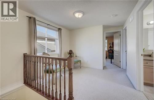 Upper-level landing featuring a wood-spindled railing, light-colored carpet flooring, and a window with neutral-toned drapes - 496 Langlaw Drive, Cambridge, ON - Indoor Photo Showing Other Room