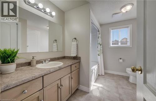Bathroom featuring a vanity with an integrated sink, a large mirror, a four-light fixture, a built-in bathtub with shower, and tile flooring - 496 Langlaw Drive, Cambridge, ON - Indoor Photo Showing Bathroom