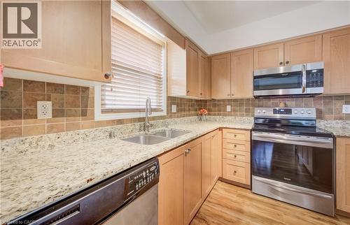 Kitchen featuring light wood cabinetry, light granite-style countertops, a mosaic tile backsplash, and stainless steel appliances including a double basin sink, dishwasher, range, and microwave - 521 Snowdrop Court, Kitchener, ON - Indoor Photo Showing Kitchen With Double Sink