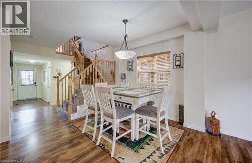 Dining area featuring wood-finish flooring, a contemporary ceiling light fixture, a window with horizontal blinds, and a staircase with wood railings - 521 Snowdrop Court, Kitchener, ON - Indoor Photo Showing Dining Room