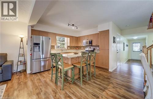 Kitchen featuring wood-finish flooring, light wood cabinetry, a center island with a light stone countertop, stainless steel appliances, and a tiled backsplash - 521 Snowdrop Court, Kitchener, ON - Indoor