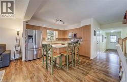 Kitchen featuring wood-finish flooring, light wood cabinetry, a center island with a light stone countertop, stainless steel appliances, and a tiled backsplash - 