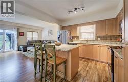 Open-concept kitchen featuring wood-finish flooring, light-toned cabinetry, and granite countertops - 