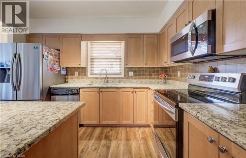 Kitchen featuring light wood-finish cabinetry, granite-style countertops, stainless steel appliances, a tiled backsplash, and wood-finish flooring - 521 Snowdrop Court, Kitchener, ON - Indoor Photo Showing Kitchen
