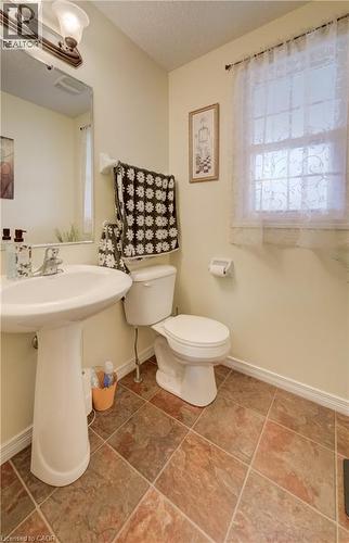 Pedestal sink with chrome faucet, complemented by a toilet and multi-toned floor tiles - 521 Snowdrop Court, Kitchener, ON - Indoor Photo Showing Bathroom