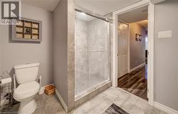 Three-piece bathroom featuring a glass-enclosed shower with tiled walls, a standard toilet, and large format tiled flooring - 
