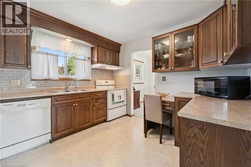 Warm wood cabinetry and countertops define this galley-style kitchen, featuring white appliances, subway tile backsplash, and ample storage with glass-front upper cabinetry - 18 Strathcona Crescent, Kitchener, ON - Indoor Photo Showing Kitchen With Double Sink