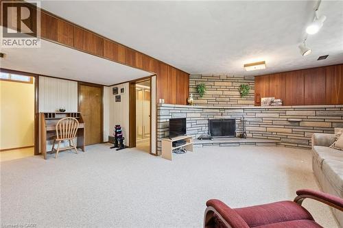 Expansive lower-level recreation room featuring wood-paneled accent walls, carpet flooring, and a brick fireplace with integrated shelving - 18 Strathcona Crescent, Kitchener, ON - Indoor
