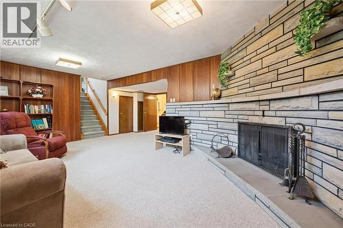 Stone-clad fireplace with a hearth and metal grate, wood paneling, built-in shelving, white carpeting, and a staircase with wood railing - 18 Strathcona Crescent, Kitchener, ON - Indoor With Fireplace